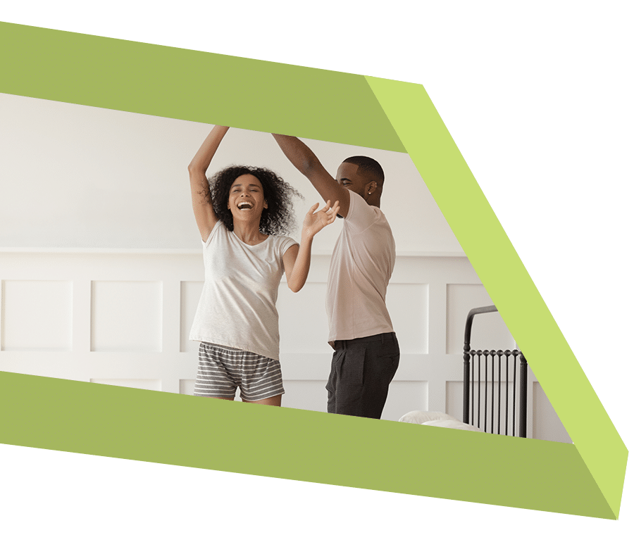 Couple wearing pajamas dancing on bed at home